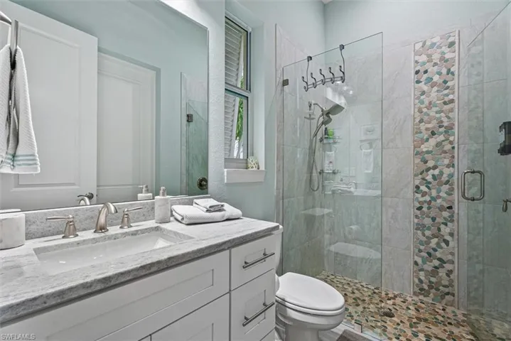 Bathroom featuring a walk-in shower with glass enclosure, pebble-tile flooring, and a decorative vertical accent tile