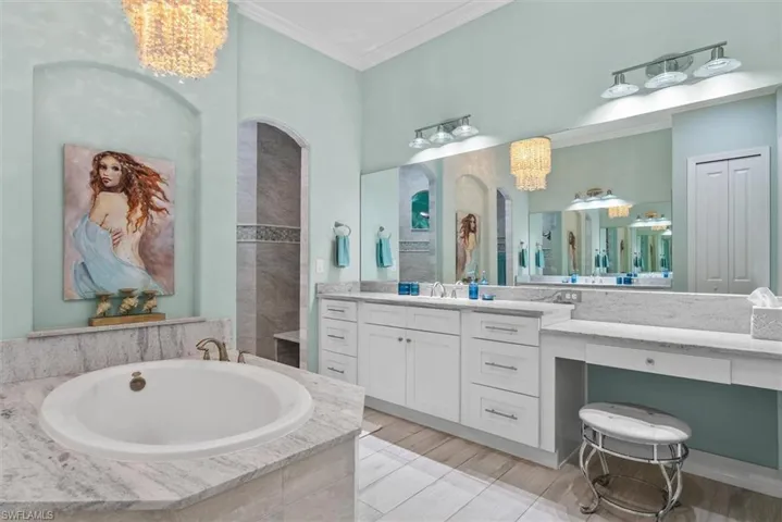Spacious bathroom featuring a built-in tub, dual vanities with white cabinetry, extensive countertop space, and a large wall-mounted mirror
