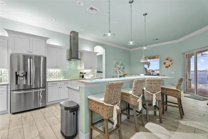 Gourmet kitchen featuring stainless steel appliances, custom white cabinetry, a glass tile backsplash, an eat-at island, and wood-finish flooring