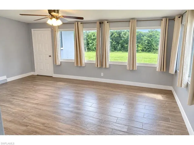 Wood-finish flooring, ceiling fan with integrated lighting, multiple windows, and a panel door