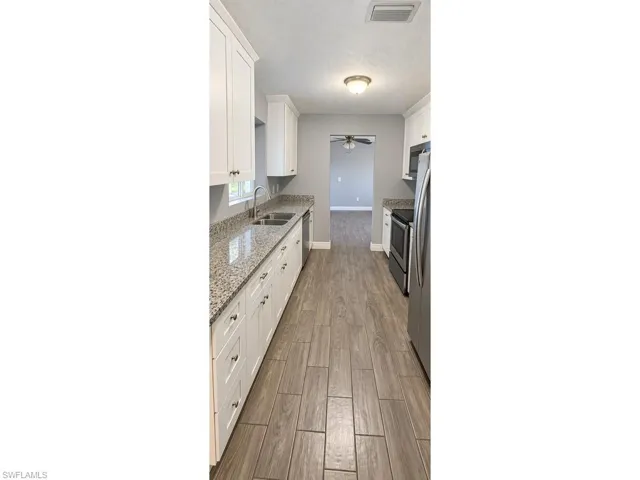 White shaker-style cabinetry, double basin sink, light-colored speckled countertops, wood-finish flooring, and stainless steel appliances