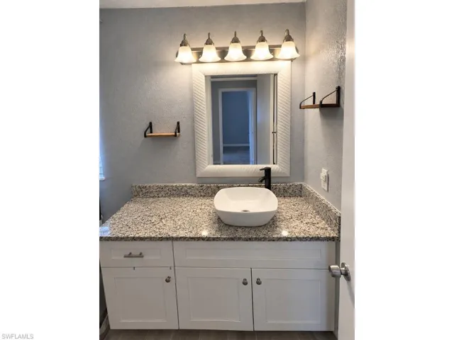White shaker-style vanity with ample storage, granite-style countertop, vessel sink, and matte black faucet