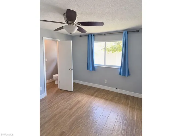 Wood-finish flooring, ceiling fan with integrated lighting, and a window with curtain rod and window treatments