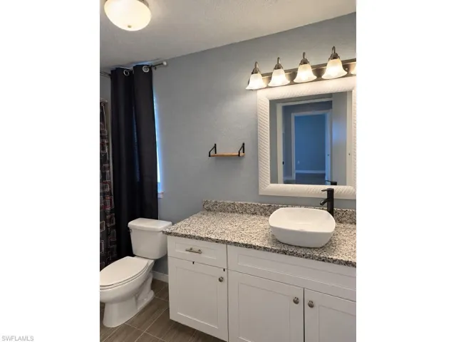 Vanity with white shaker cabinetry, speckled countertop, and a vessel sink with a matte black faucet