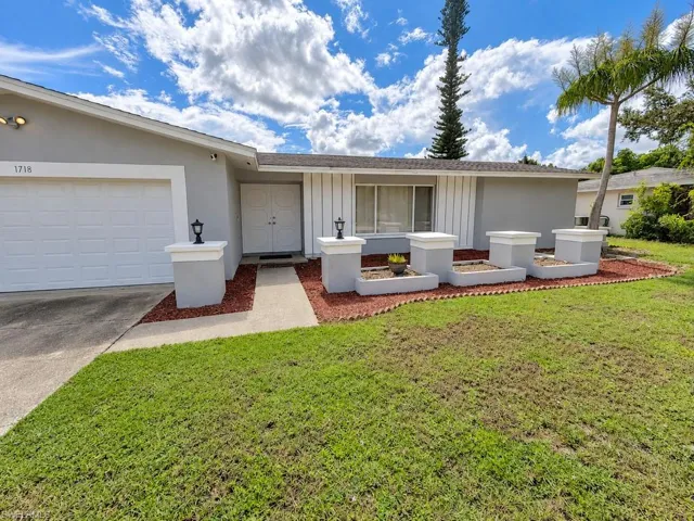 Single-story residence featuring a garage, double entry doors, front landscaping with decorative planters, and a concrete walkway