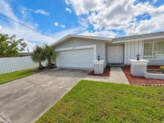 Exterior featuring a white garage door, double entry doors, decorative outdoor lighting, and a mature palm tree