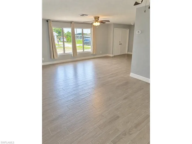 Light-toned plank tile flooring, multiple large windows, and a ceiling fan with integrated lighting
