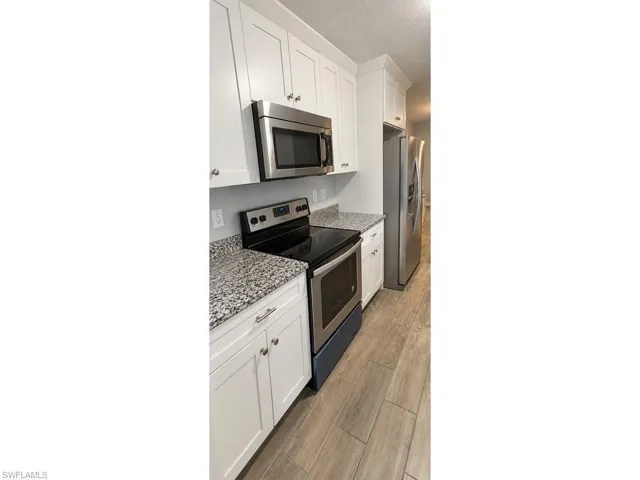 White cabinetry, stainless steel appliances, granite countertops, and wood-finish flooring