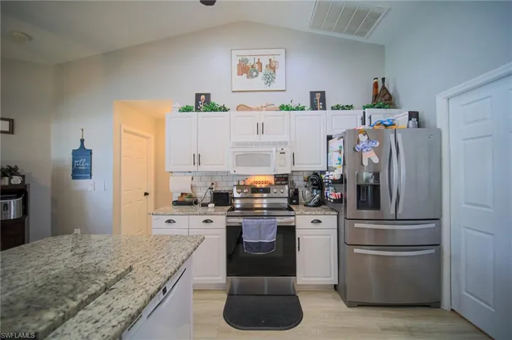 Kitchen featuring stainless steel appliances, white cabinetry, vaulted ceiling, and light wood-type flooring