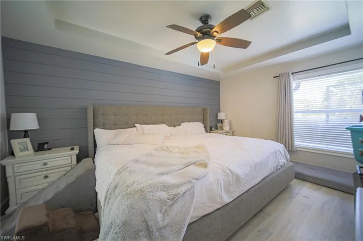 Bedroom featuring a raised ceiling, light wood finished floors, a ceiling fan, and wooden walls