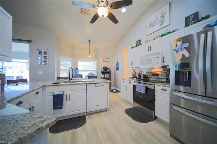 Kitchen with stainless steel appliances, vaulted ceiling, white cabinetry, a ceiling fan, and light wood-style floors