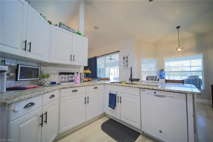 Kitchen featuring white dishwasher, backsplash, light wood finished floors, a peninsula, and white cabinets