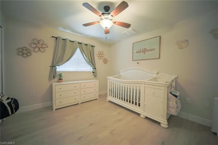 Bedroom with light wood-style flooring, a nursery area, and a ceiling fan