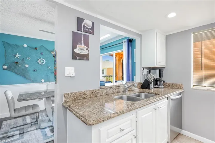 Kitchen with light stone countertops, stainless steel dishwasher, white cabinets, sink, and a textured ceiling
