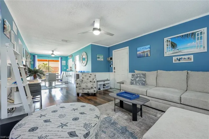 Living room featuring a textured ceiling, dark hardwood / wood-style floors, ornamental molding, and ceiling fan