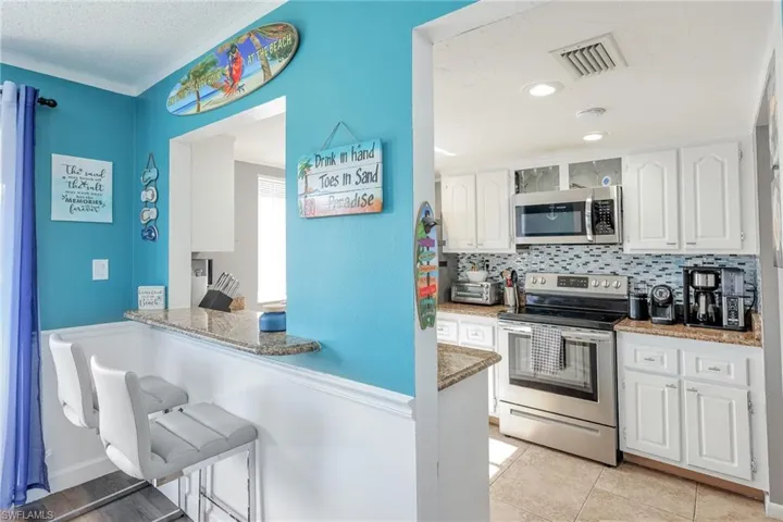 Kitchen with kitchen peninsula, backsplash, light tile floors, white cabinetry, and appliances with stainless steel finishes