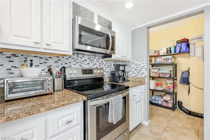 Kitchen with appliances with stainless steel finishes, white cabinets, tasteful backsplash, and light stone countertops