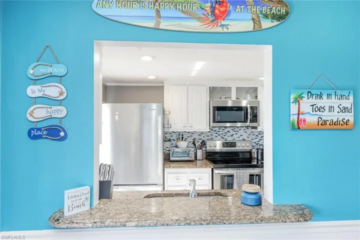 Kitchen with light stone countertops, appliances with stainless steel finishes, white cabinets, backsplash, and sink