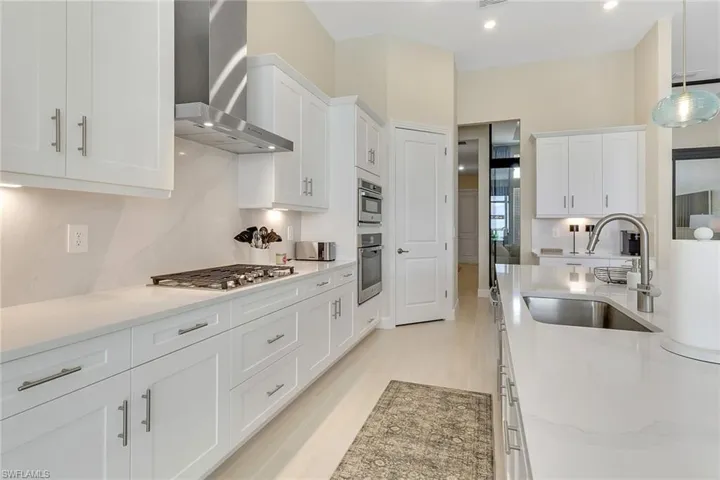 Kitchen featuring hanging light fixtures, white cabinetry, wall chimney exhaust hood, light stone countertops, and recessed lighting