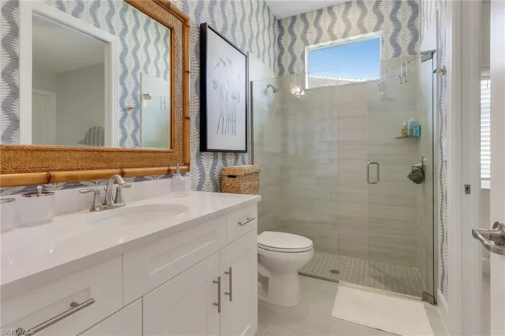 Bathroom featuring wallpapered walls, vanity, a shower stall, and light tile patterned flooring