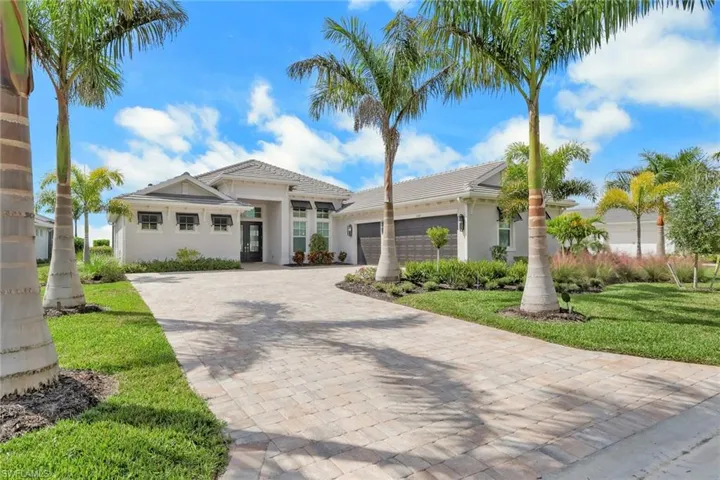 View of front of property featuring an attached garage, decorative driveway, a front lawn, and stucco siding