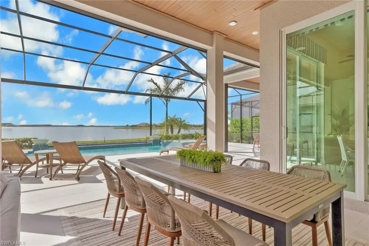 View of patio / terrace with a sunroom, glass enclosure, an outdoor pool, outdoor dining space, and a water view