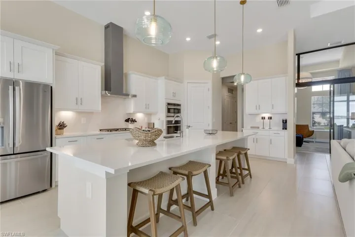 Kitchen with appliances with stainless steel finishes, a kitchen breakfast bar, a large island with sink, white cabinets, and wall chimney exhaust hood