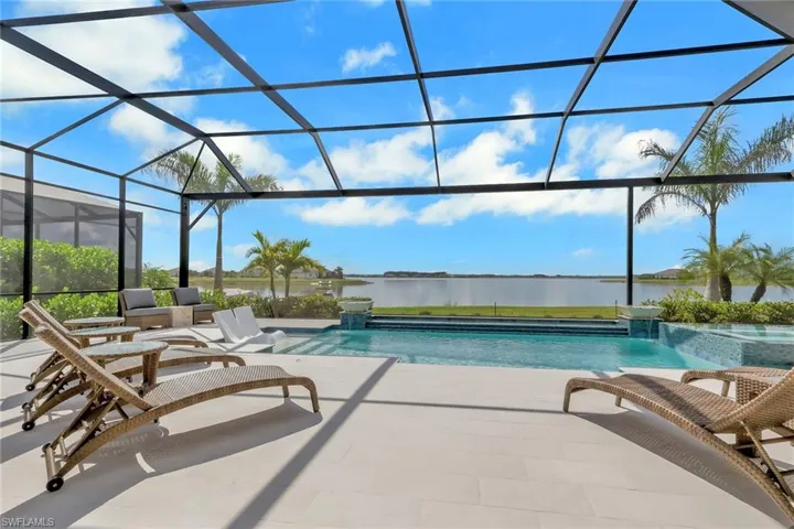 View of swimming pool with a sunroom, glass enclosure, a pool with connected hot tub, a patio area, and a water view