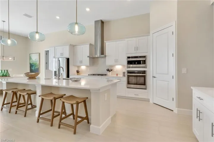 Kitchen with a breakfast bar area, white cabinetry, an island with sink, decorative light fixtures, and stainless steel appliances
