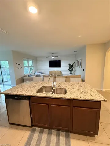 Kitchen with ceiling fan, an island with sink, dishwasher, a sink, and open floor plan