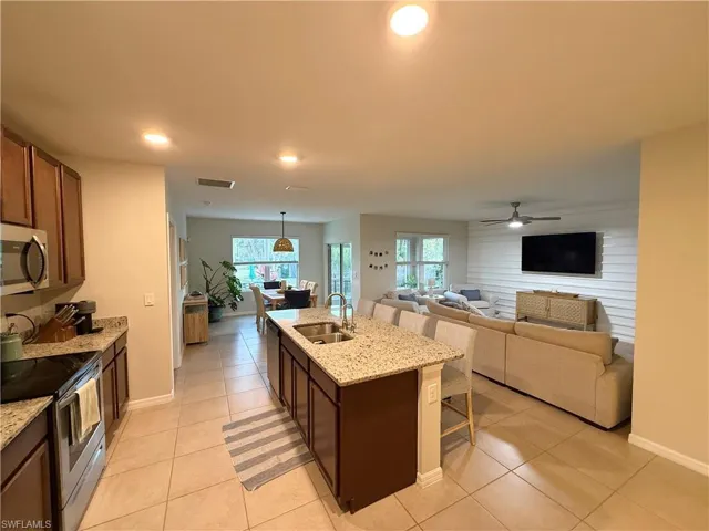 Kitchen with light tile patterned floors, a sink, a kitchen breakfast bar, a kitchen island with sink, and stainless steel appliances