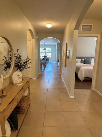 Hallway featuring light tile patterned flooring, visible vents, baseboards, and arched walkways