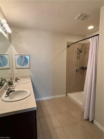 Bathroom with a tile shower, a sink, tile patterned floors, and baseboards