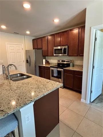 Kitchen with fridge, light stone counters, stainless steel range with electric cooktop, light tile patterned floors, and a sink