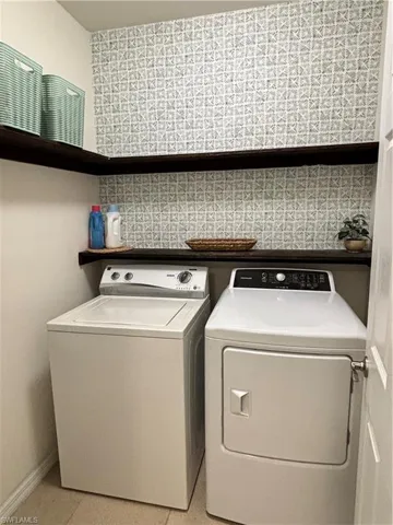 Washroom featuring light tile patterned floors, washing machine and dryer, laundry area, and baseboards