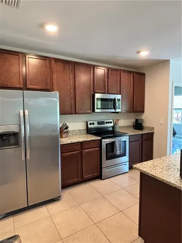 Kitchen with stove, light stone countertops, light tile patterned floors, and fridge