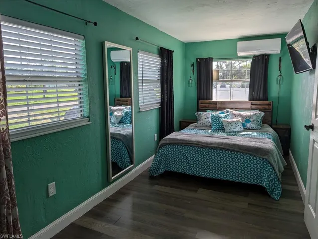 Bedroom featuring a wall unit AC, wood finished floors, and a textured wall