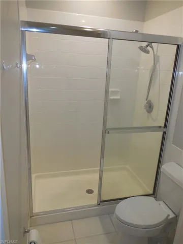 Bathroom featuring a shower with shower door, toilet, and tile patterned flooring