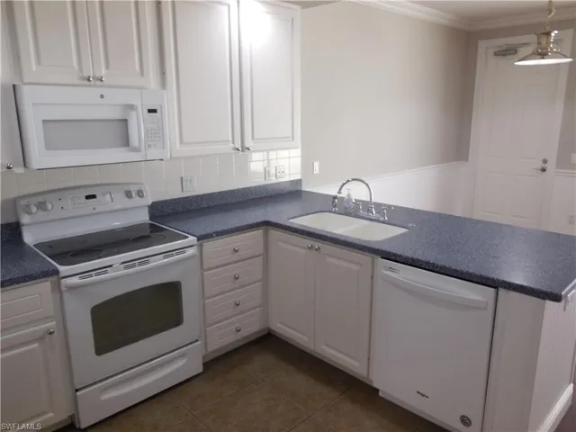 Kitchen featuring white cabinets, dark tile patterned flooring, white appliances, sink, and ornamental molding