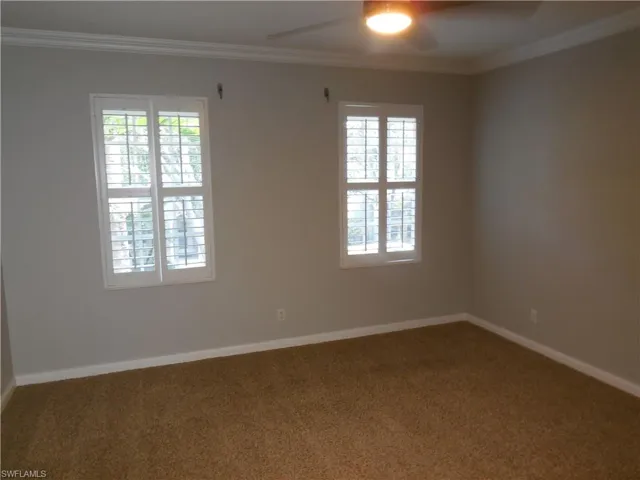 Carpeted empty room featuring ceiling fan, a healthy amount of sunlight, and crown molding