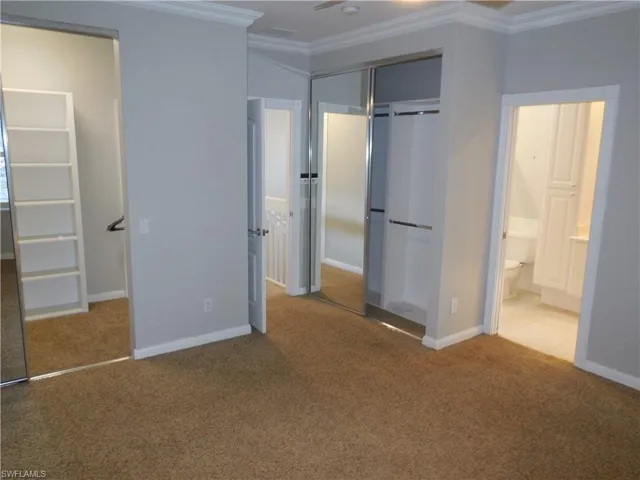 Unfurnished bedroom with crown molding, ensuite bath, a closet, and carpet