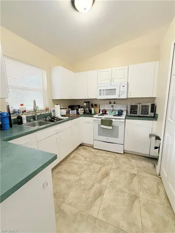 Kitchen featuring white appliances, dark countertops, white cabinetry, and lofted ceiling