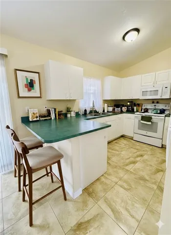 Kitchen with a breakfast bar area, white appliances, white cabinetry, a peninsula, and lofted ceiling
