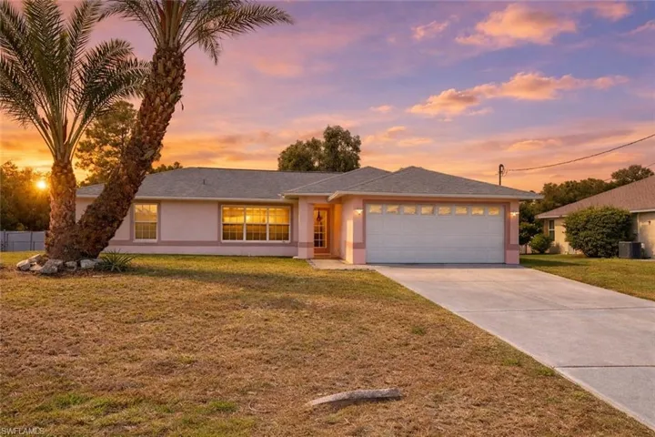 View of front of home with stucco siding, a front lawn, concrete driveway, a garage, and roof with shingles