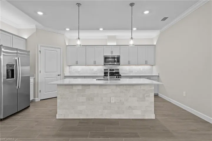 Kitchen featuring appliances with stainless steel finishes, a kitchen island with sink, wood finished floors, a sink, and light countertops