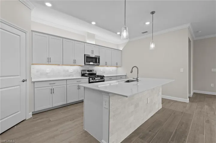 Kitchen featuring stainless steel appliances, a sink, light wood-style floors, decorative backsplash, and ornamental molding