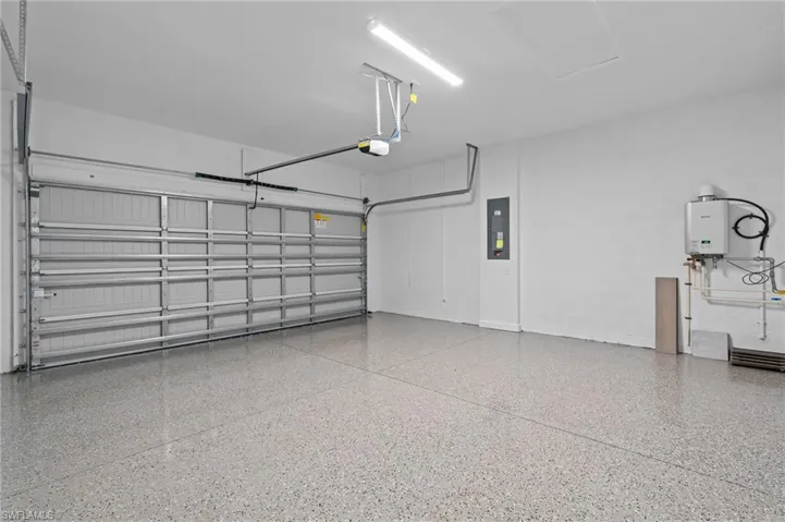 Garage with electric panel, a garage door opener, and tankless water heater