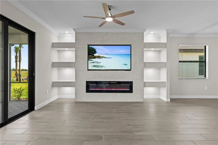 Unfurnished living room featuring baseboards, built in features, a fireplace, wood finished floors, and ornamental molding