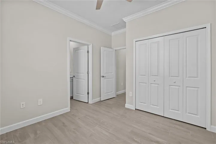 Unfurnished bedroom with crown molding, light wood finished floors, baseboards, a closet, and a ceiling fan