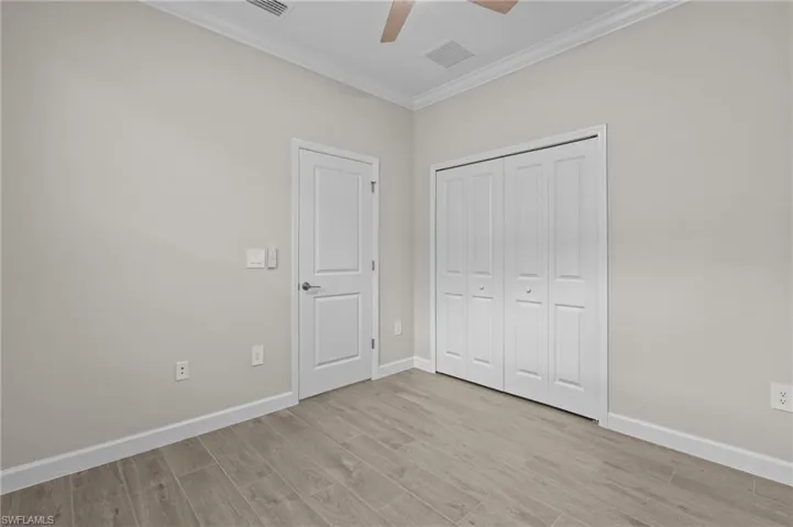 Unfurnished bedroom featuring crown molding, light wood-style floors, baseboards, a closet, and ceiling fan